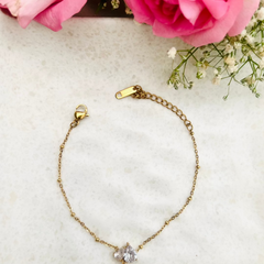 Gold bracelet with a diamond pendant on a light surface with pink roses and baby's breath.
