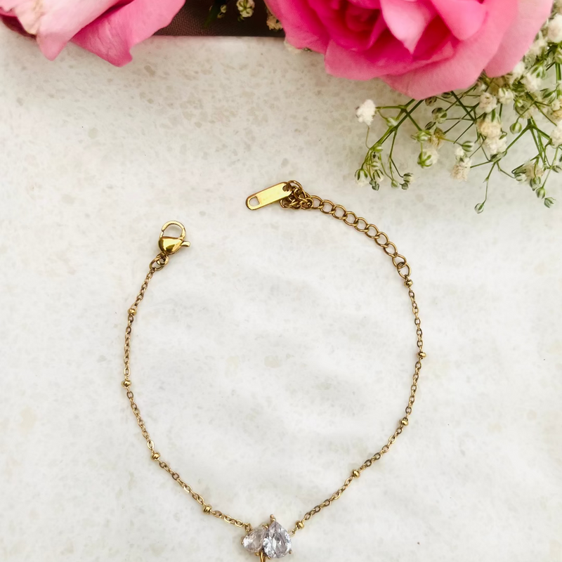 Gold bracelet with a diamond pendant on a light surface with pink roses and baby's breath.
